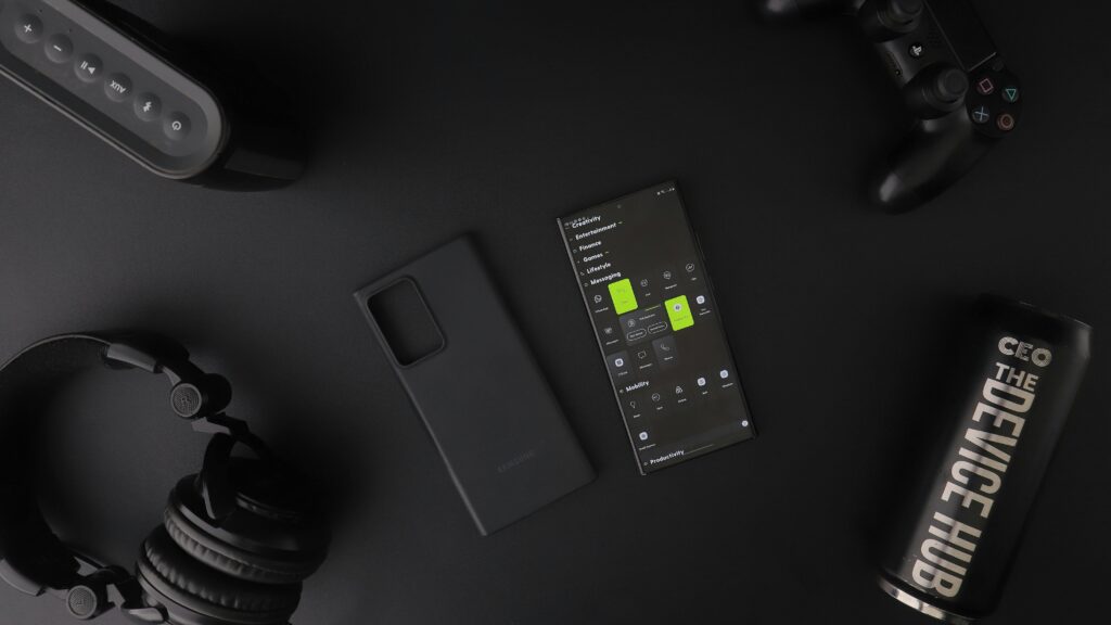 Overhead view of black modern electronics including smartphone, headphones, speaker, and controller on a table.